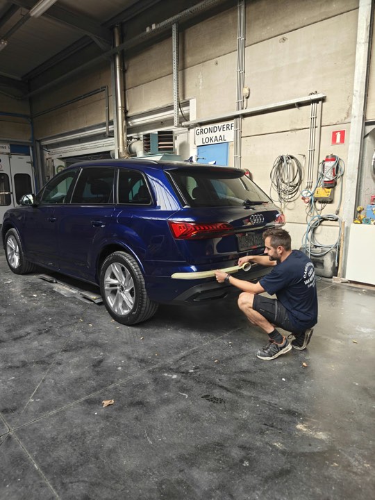 Carrossier plakt de bumper van een blauwe Audi Q7 af