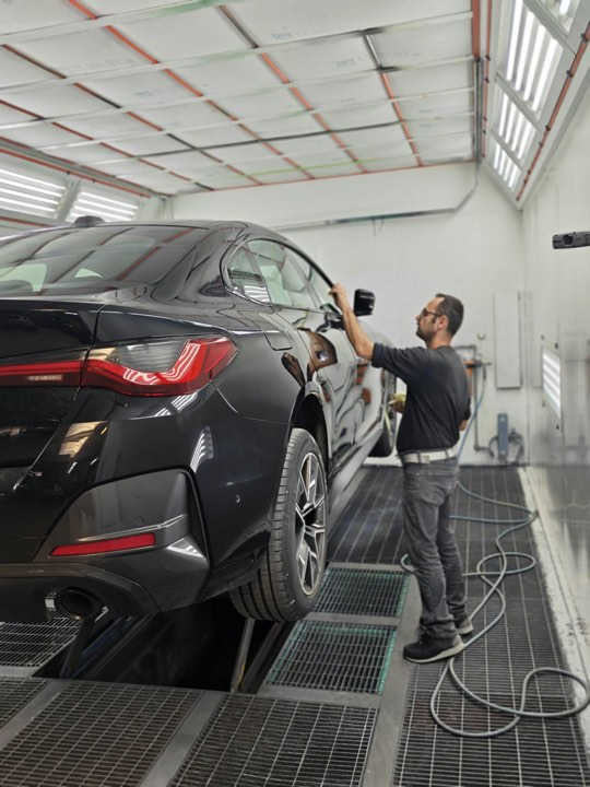 Carrossier bij een zwarte BMW in de spuitcabine